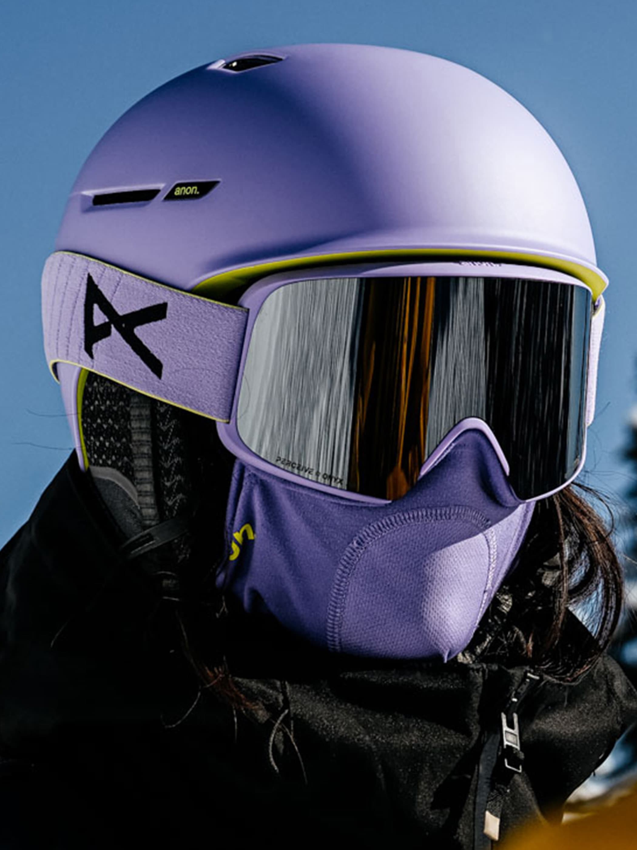 Person wearing a purple helmet and goggles and facemask with a clear blue sky.